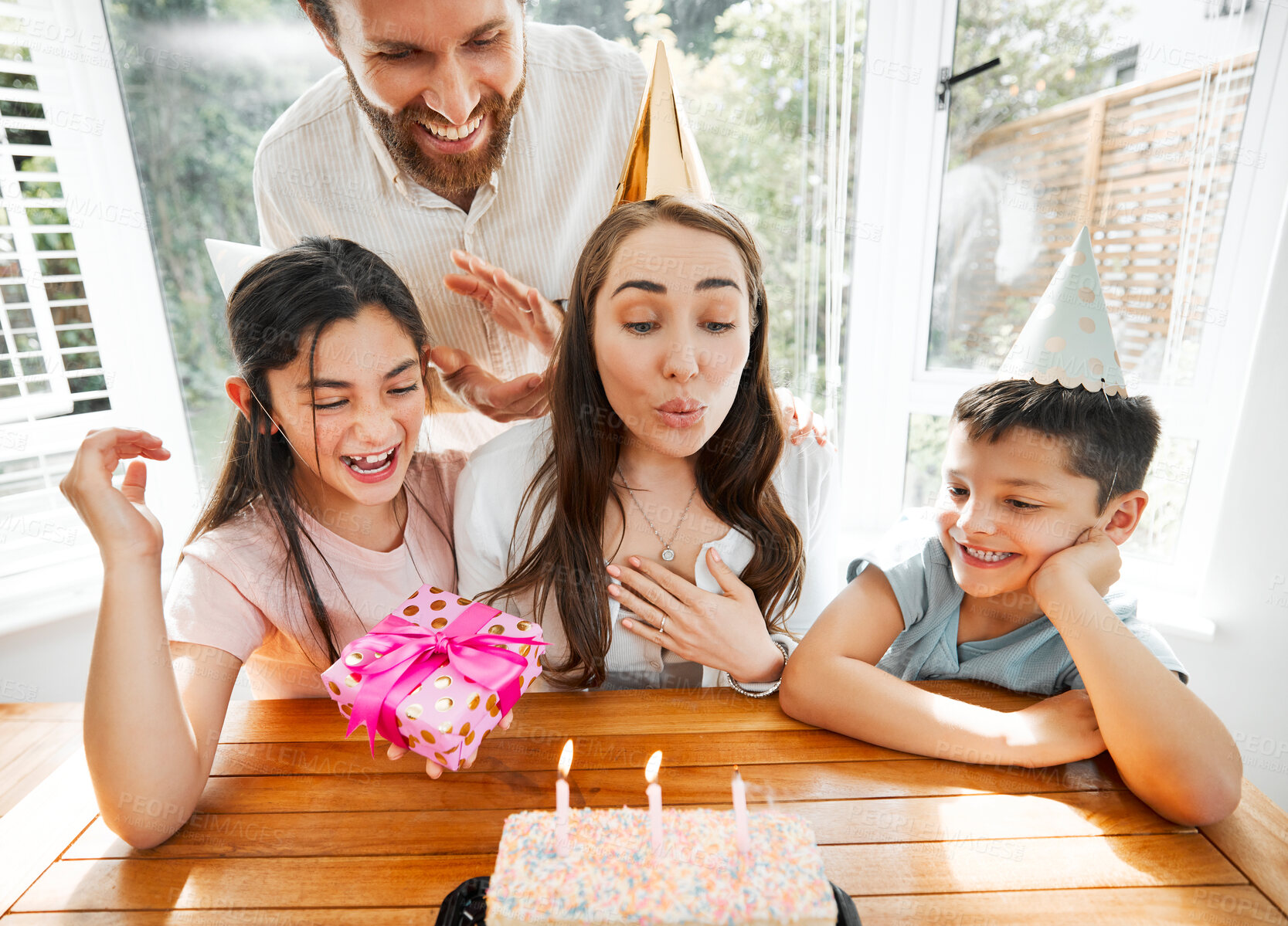 Buy stock photo Birthday, family and celebration with a woman blowing the candles on her cake. Husband and kids spoiling mom and making her feel happy on her special day mothers day while having a party at home
