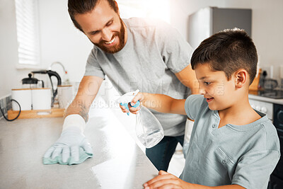 Buy stock photo Father teaching young son cleaning chores in the family home having fun and bonding together. Smiling and loving father helping, washing and wiping kitchen counter with his little boy indoors