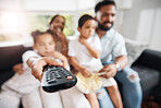 Closeup of remote control with family watching tv in their living room together. Parents and kids relaxing on the sofa enjoying a movie, series or cartoons in the loung at home while bonding