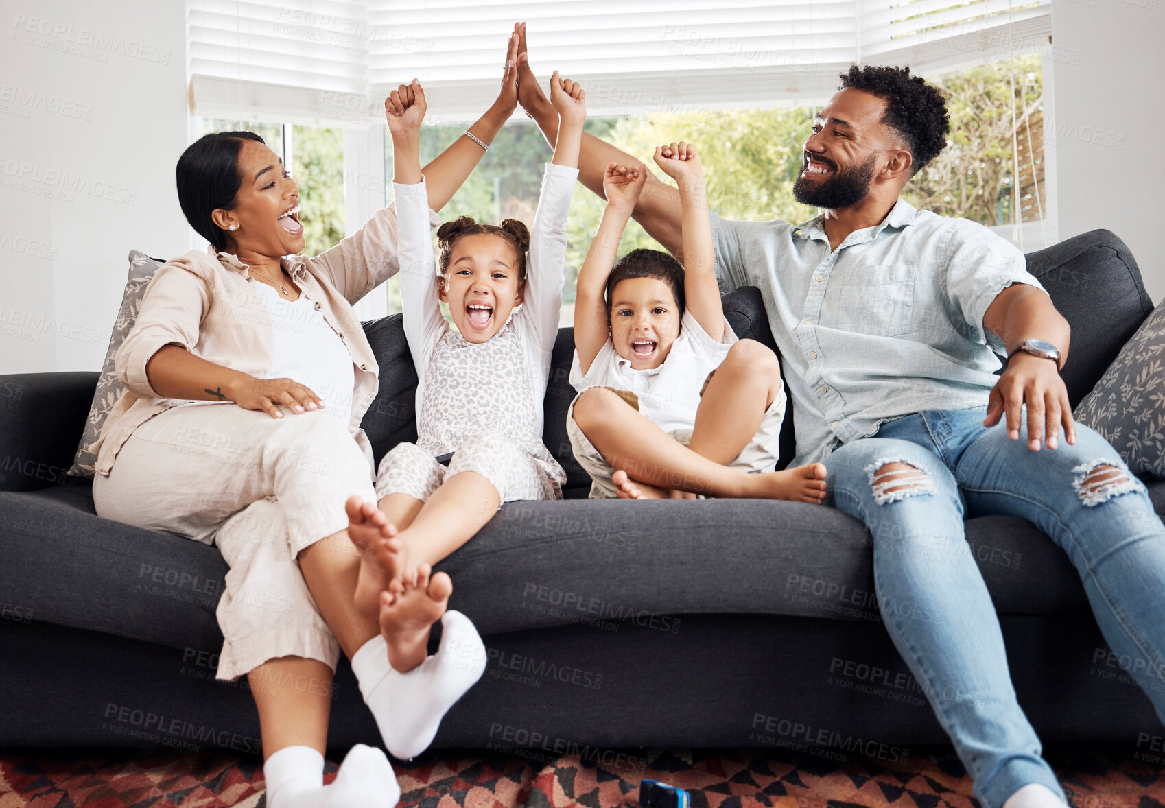 Buy stock photo Happy parents and excited children celebrate on the sofa while watching tv. Fun family time, relaxing at home and bonding. Mother and father high five, kids cheer for sports team win.