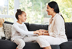 Happy, smiling and talking mother and daughter bonding, holding hands and showing affection while relaxing on the couch together at home. Little, innocent and young girl enjoying a day with parent