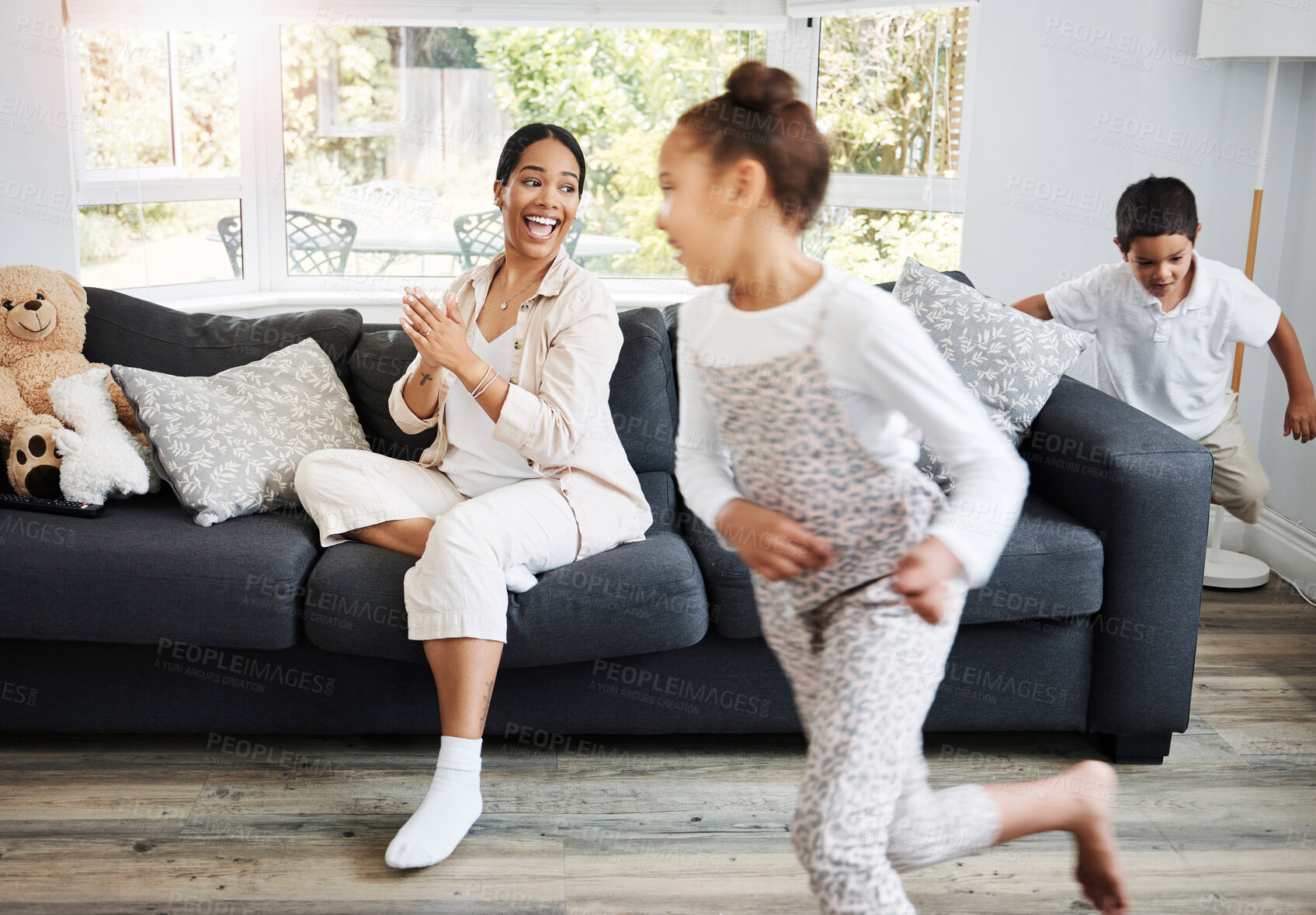 Buy stock photo Playing, running and young children excited indoors with a smiling mother watching on a couch. Happy family spending the day together indoors while the active kids run, play and have fun at home