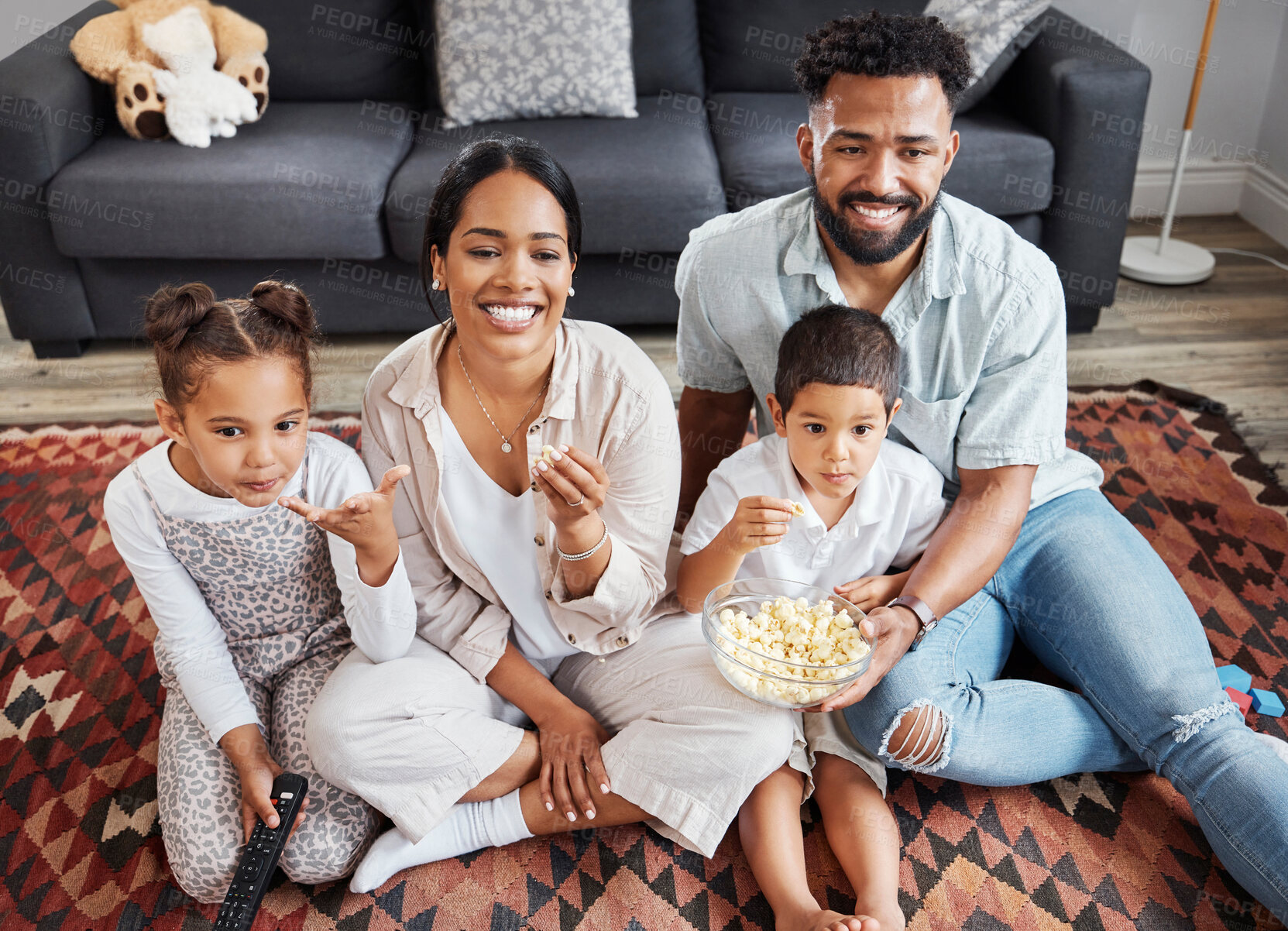Buy stock photo Watching movie, family bonding and eating popcorn while relaxing in the lounge together at home. Happy, smiling and carefree parents enjoying snack, looking at comedy series, laughing with kids