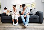 Sad, unhappy and stressed parents sitting on a couch near their children at home after an argument. Frustrated, worried and annoyed mom and dad are angry at each other in front of their kids