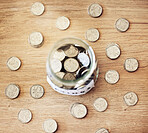 Savings, investment and a jar full of coins on a wooden table for future financial growth or insurance. Overhead view of an overflowing container with money for a donation or retirement fund