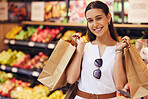 Grocery shopping, food and diet with a young woman in a retail, convenience store or grocer and fruit and vegetables in the background. Portrait of a female with paper bags in a fresh produce aisle