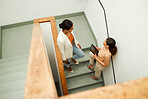 Colleagues discuss, plan and share ideas on a staircase at work in a startup business. Overhead of Businesswomen talking, chatting and socializing on a stairway during a break at a corporate job 