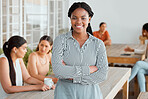Motivated, ambitious and confident young business woman standing arms crossed in the office break room with colleagues in the background. Portrait of a professional female feeling happy and positive