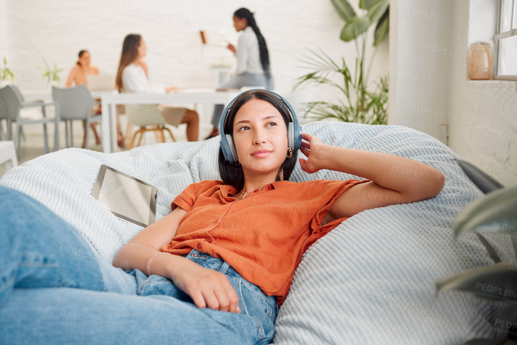 Buy stock photo Creative wearing headphones, listening to music and relaxing with zen songs or podcast to help with thinking, planning and inspiration. Motivated, inspired and ambitous woman lying on office bean bag