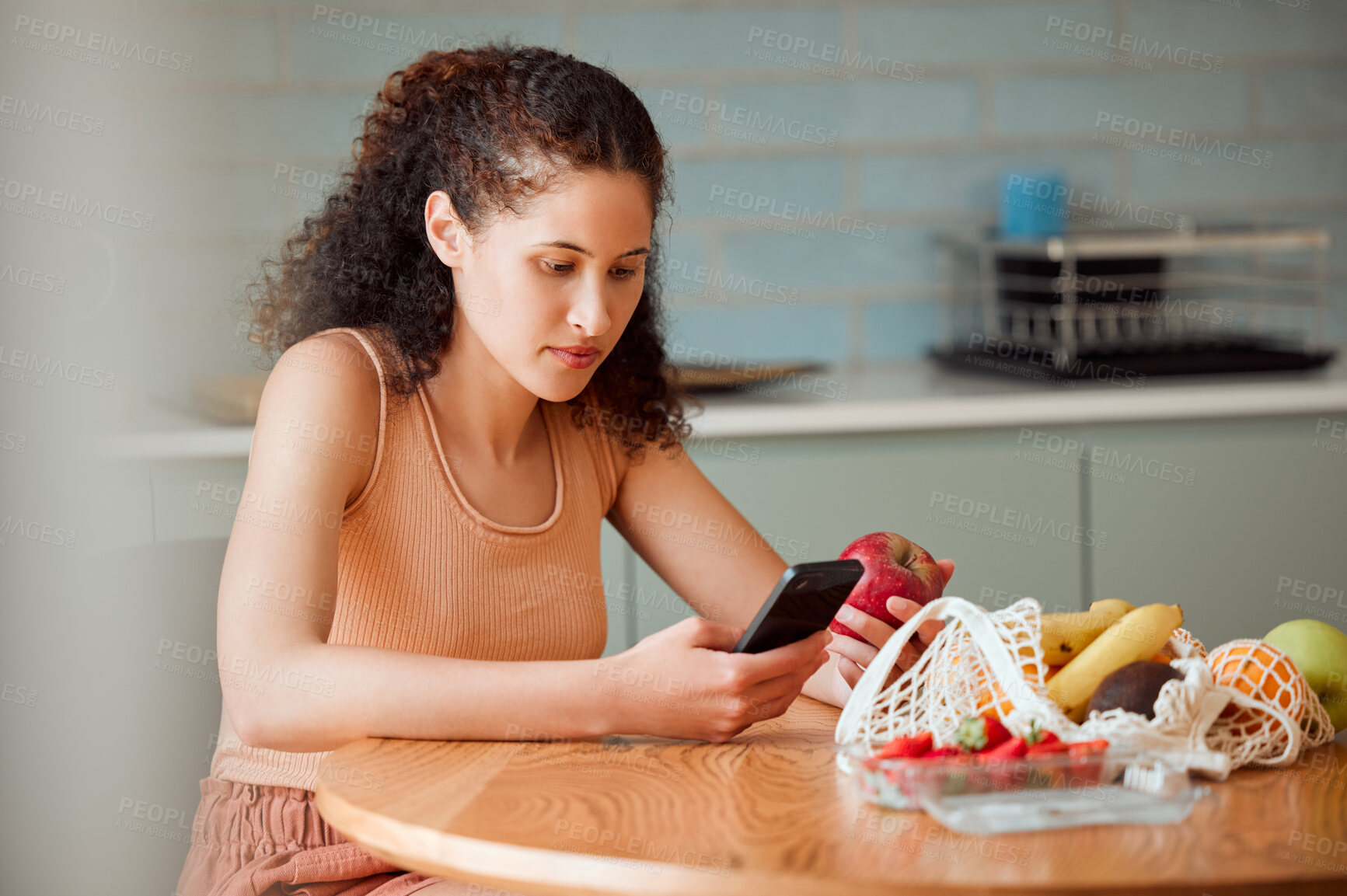 Buy stock photo Diet, healthy mindset and health food of a female doing apple research on a phone.Young woman nutritionist at home reading weight loss, cooking and nutrition holding online fruit in a kitchen 