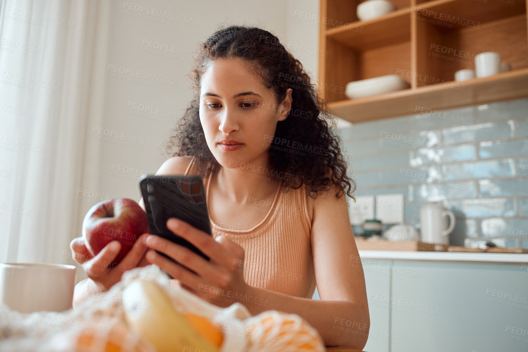 Buy stock photo Eating healthy, diet planning and personal online female dietitian. Serious nutritionist check phone, snack on fresh fruit and concentrating on social media. Communicate with patient about calories.