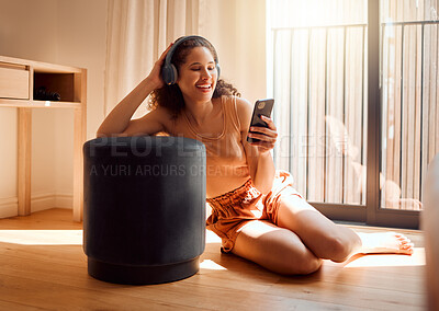 Buy stock photo Carefree, relaxed and happy woman relaxing on a video call using her phone and headphones while sitting on the floor. A young excited female listening to an online podcast or browsing social media