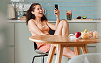 Woman browsing on phone reading social media post with an online app while relaxing in the kitchen. Female relaxing, smiling and enjoying a funny post, video or meme on the internet in the morning 