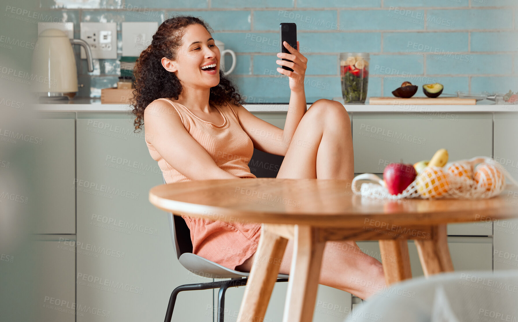 Buy stock photo Woman browsing on phone reading social media post with an online app while relaxing in the kitchen. Female relaxing, smiling and enjoying a funny post, video or meme on the internet in the morning 