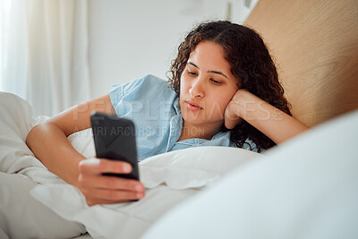 Buy stock photo Young woman checking phone and social media in bed, browsing internet after waking up to text message at home. Female relaxing, chatting online and streaming. Lady feeling lazy on the weekend