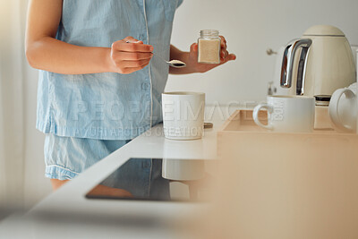 Buy stock photo Casual woman adding sugar while preparing a cup of coffee, tea or hot chocolate in the kitchen during the morning. Female hands holding teaspoon for a fresh beverage in a mug for breakfast at home
