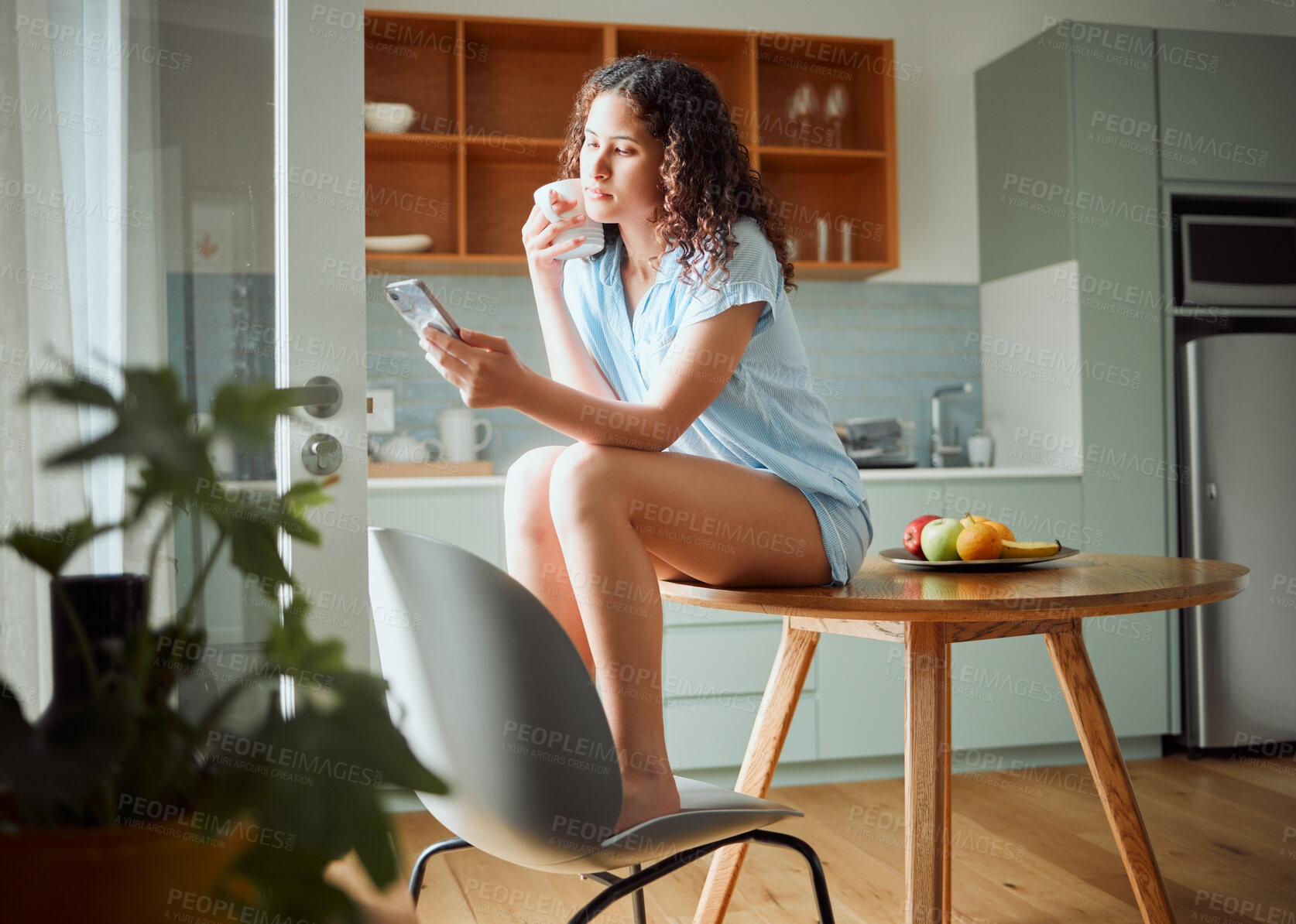 Buy stock photo Woman browsing social media on phone, drinking cup of coffee and relaxing in the morning at home. Relaxed, content and serious female browsing the internet, posting on status online and chatting