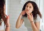 Unhappy, upset or annoyed woman popping a zit during a skincare routine while in front of a mirror in the bathroom. Young lady with a pimple targeting acne, dry skin or pimple on her face at home