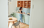 Young woman making tea, coffee or warm drink in a kitchen while relaxing at home. Female enjoying, preparing and drinking warm beverage for a cosy, comfortable and peaceful morning, day or breakfast