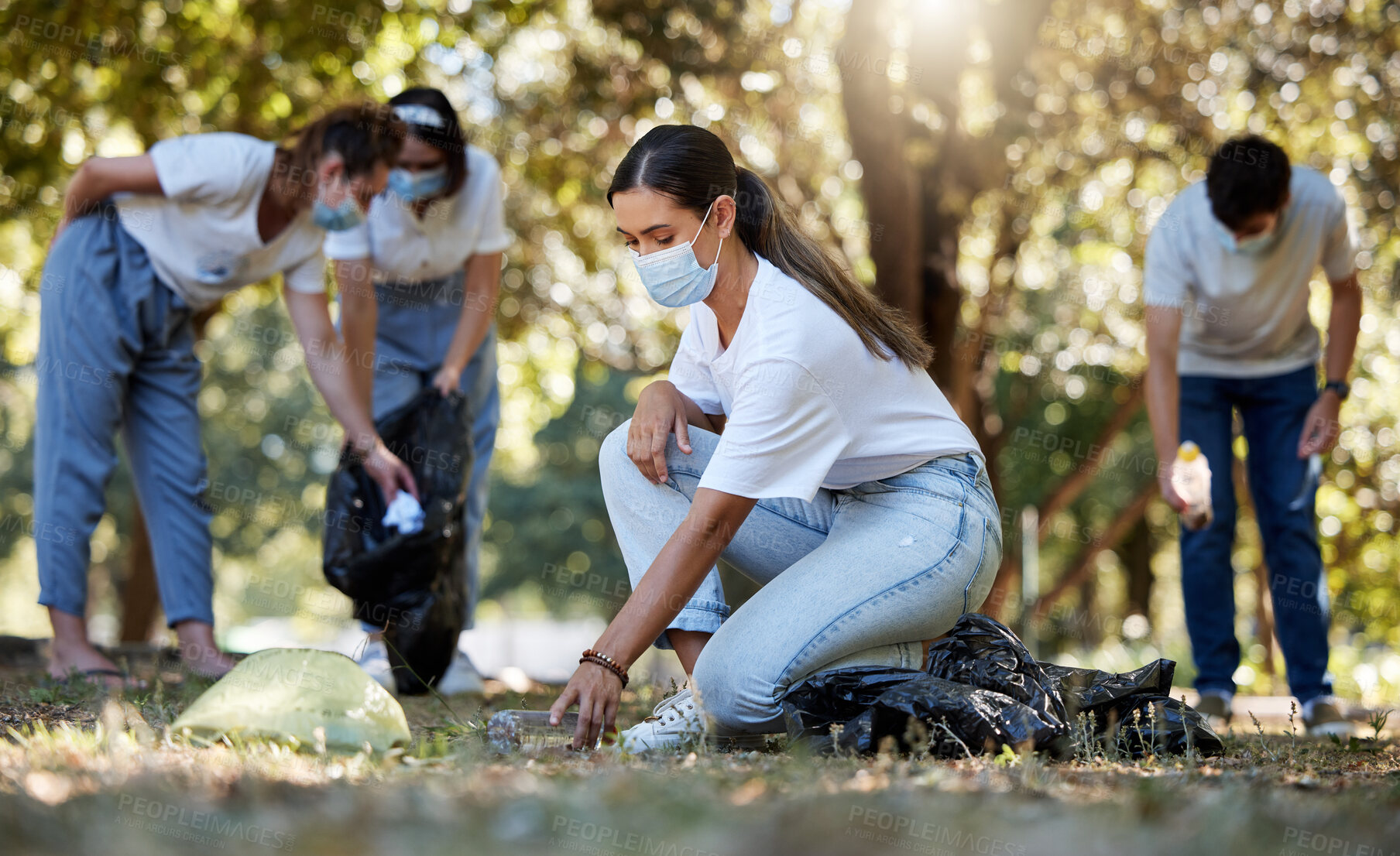 Buy stock photo Group of volunteers picking up, cleaning and reducing pollution in a public nature park together. Diverse community wearing face masks to protect from disease, collecting dirt and doing cleanup