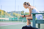 Fit sports woman with phone checking fitness goal progress on a modern exercise app online while taking a break at the tennis court. A sportswoman checking messages on cellphone and waiting for coach