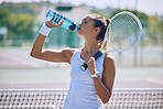 Fit and active tennis player drinking water from a bottle after practicing, training and playing on a sports court or club. Thirsty professional sportswoman hydrating while holding a racket outside
