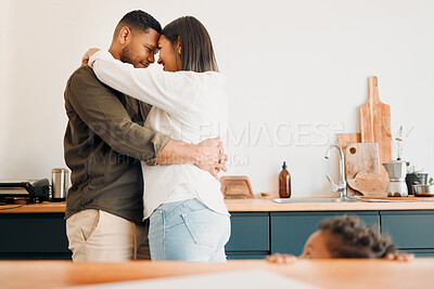 Buy stock photo Cosy couple hugging, romance and affection in a modern kitchen with small child looking at them. Loving, young and parents, mom and dad embrace, excited by the future of their growing family