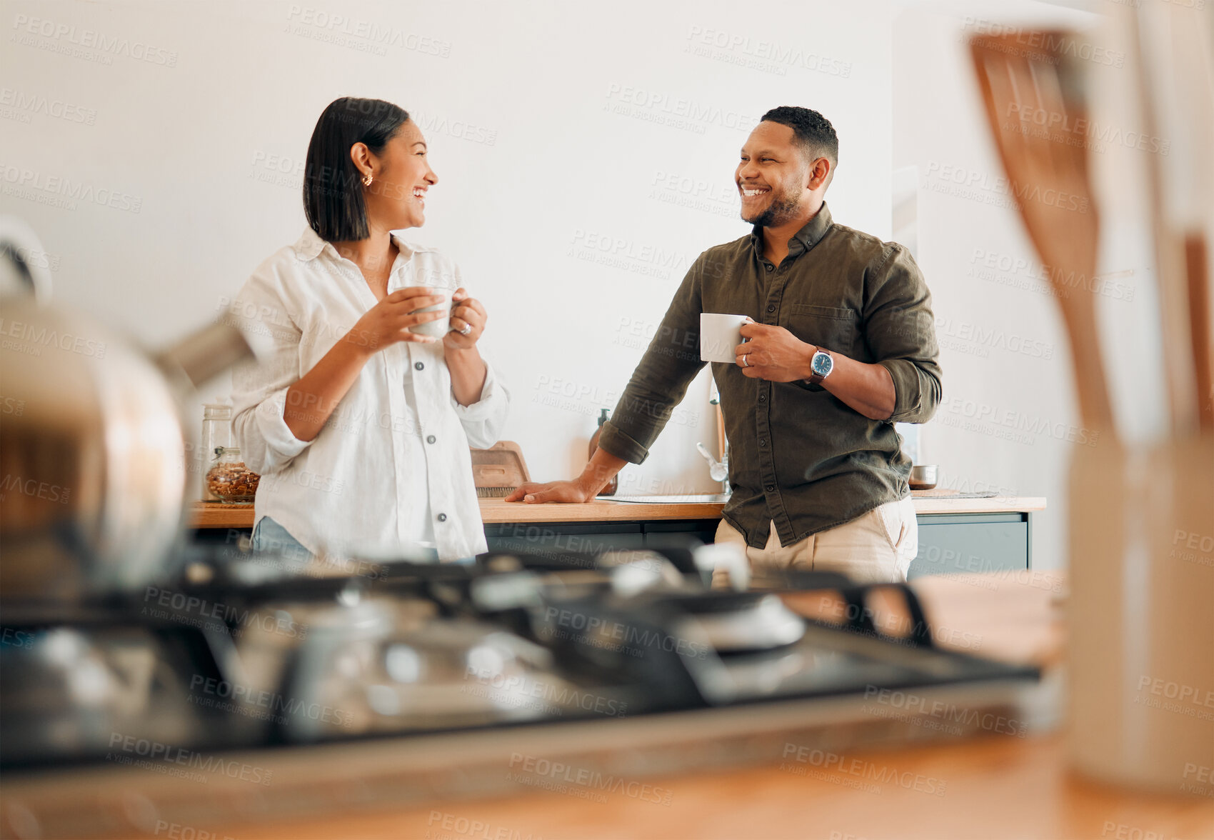 Buy stock photo Loving couple drinking coffee and talking, bonding and having fun while spending time together at home. Smiling, in love and carefree couple hugging and sharing a romantic moment enjoying the morning