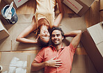 Home improvement, renovation and remodeling with a young couple lying on the floor together at home from above. Man and woman homeowners moving house, painting and unpacking boxes or packages