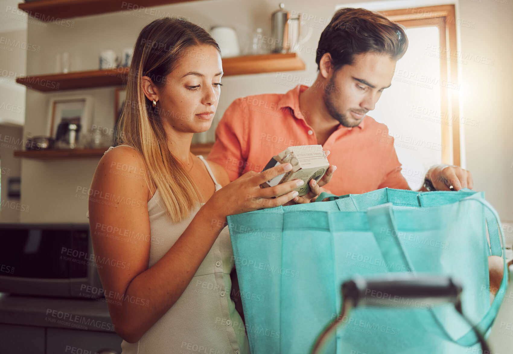 Buy stock photo Groceries, plastic free and healthy couple unpacking after returning home from a shopping trip. Serious man and woman with reusable bag with food and ingredients while reading nutritional labels 