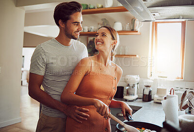 Buy stock photo Romantic, happy and young couple cooking dinner food and hug on a home date in a kitchen. Smiling dating partners relax feeling happiness, romance and love spending time at their house or apartment
