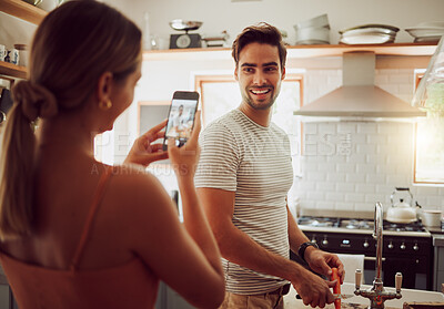 Buy stock photo Woman taking photo with phone of boyfriend in the kitchen while bonding, laughing and cooking together. Fun, happy and loving couple enjoy preparing meal together and taking picture for social media