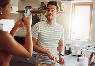 Buy stock photo Silly, goofy and interracial couple taking pictures, having fun and cooking together in the kitchen at home. Happy girlfriend taking pictures of boyfriend, making funny faces and preparing dinner