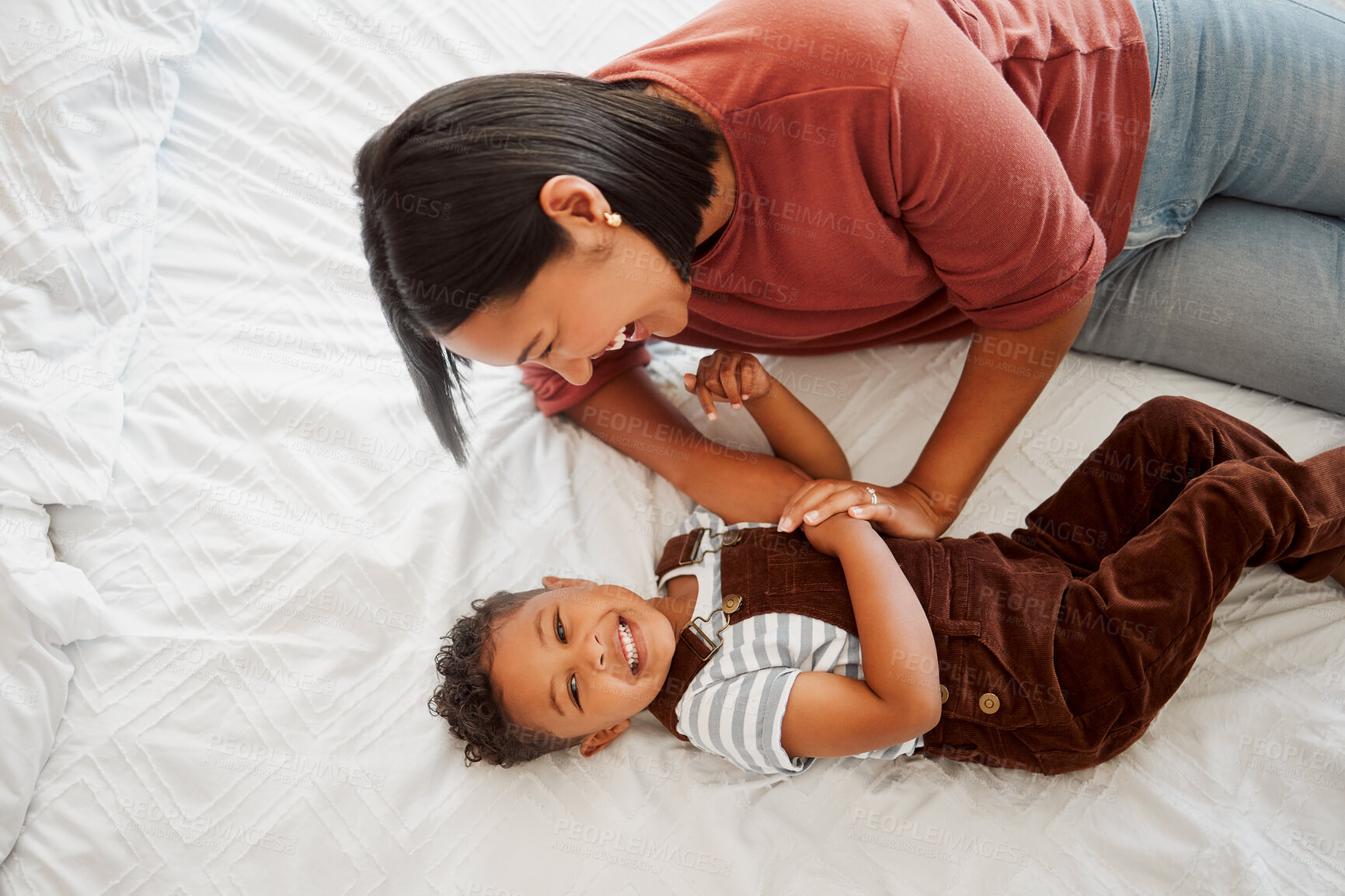 Buy stock photo Playful, fun and funny mother playing and bonding with her son laughing together on a bed at home from above. A single mom enjoying quality time and parenting her child or kid in the bedroom