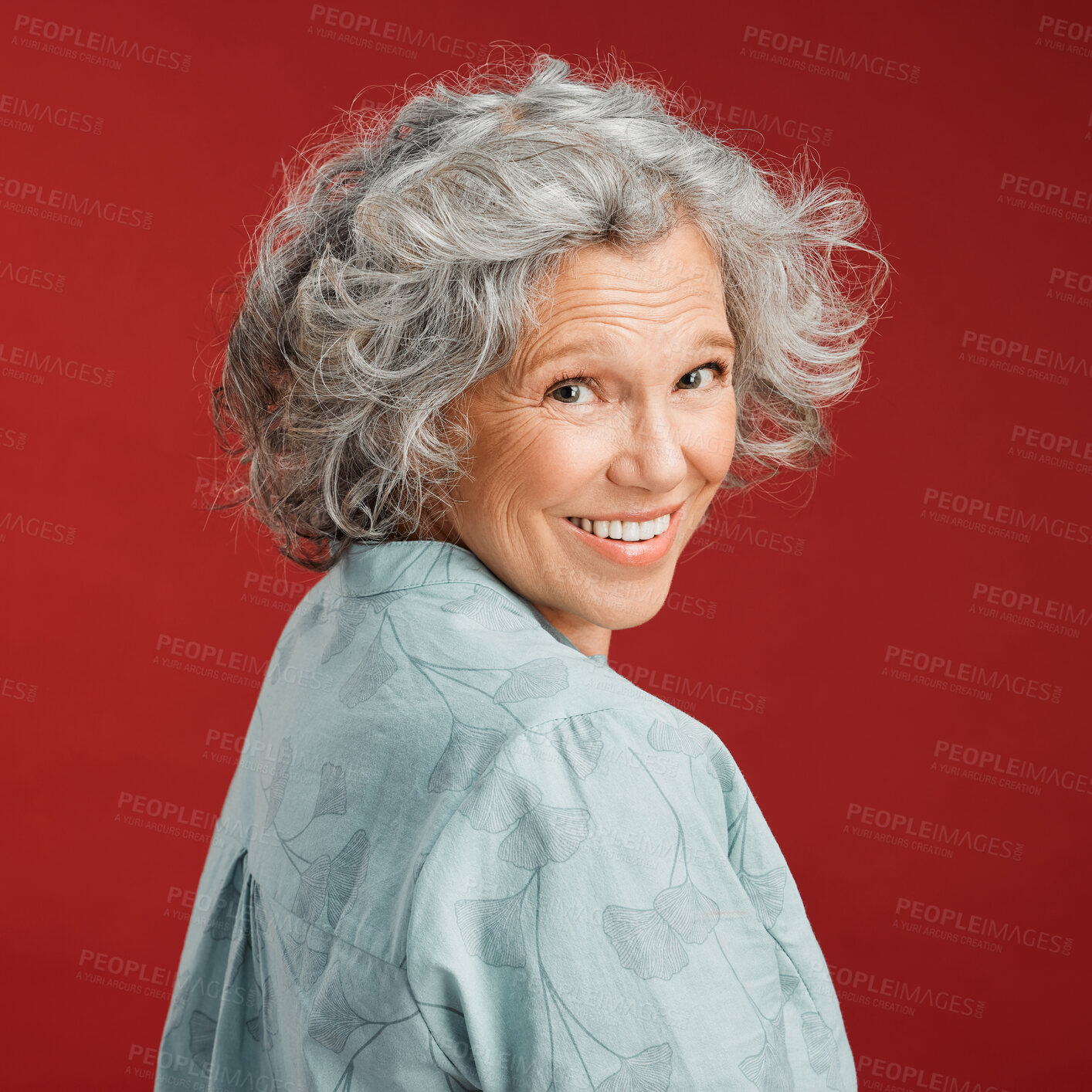 Buy stock photo Confident, happy and smiling senior woman feeling playful and cheerful while posing against red studio background. Portrait of a beautiful, older and retired lady looking back with grey hair