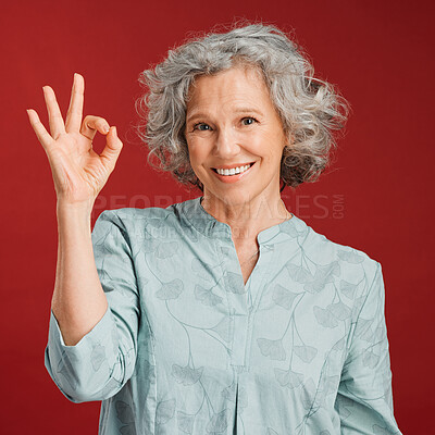 Buy stock photo Good, perfect and okay with a senior woman hand gesture or sign in support or positive backing in studio against a red background. Portrait of a mature female looking motivated, happy and smiling