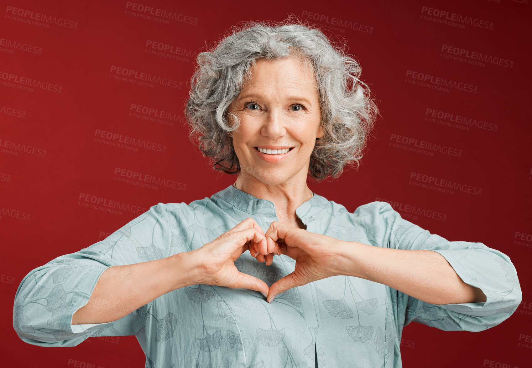 Buy stock photo Love, heart and health retired woman with loving emoji sign, icon or symbol showing care or affection on red valentines day studio background. Grey, senior or pensioner with a trendy emoticon pose