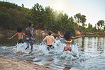 Excited, carefree and fun group of friends enjoying outdoors nature swimming trip together by the lake. Young joyful People making a splash in swimwear or bikini, on their holiday summer vacation