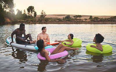 Buy stock photo Diverse friend group floating on lake water, having fun in nature and bonding on a vacation in countryside sunset with inflatable rings. Men and women laughing, smiling and looking relaxed on holiday