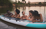 Friends, vacation and having fun while leaning on a paddle board and talking in a lake. Happy and diverse people laughing while enjoying the water and friendship on their holiday and nature travel
