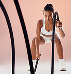 Fitness, battle ropes and active woman in a routine workout, training and exercise against pink studio background. Sporty, athletic and strong athlete exercising for cardio health and muscle strength