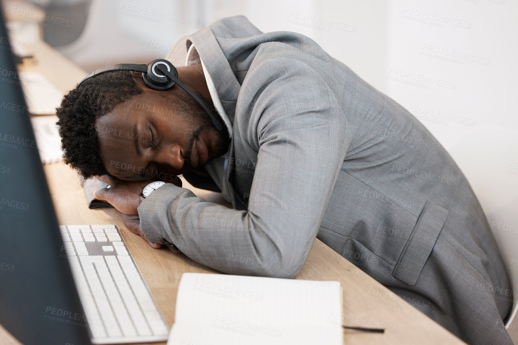 Buy stock photo Tired CRM call center agent sleeping on computer desk at work office with headset on. Exhausted young business man taking a nap on table. African American male feeling burnout resting in workplace.