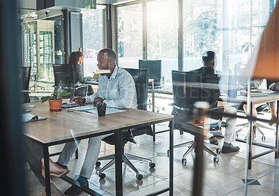 Buy stock photo Business, office and work with a man sitting at his desk in a glass building and working with colleagues in the background. A busy corporate company with an employee and worker at a table for his job