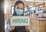 Business woman advertising a hiring sign in her startup coffee shop door. Entrepreneur, business owner or manager wearing a mask searching for employee or workers in a cafe during covid pandemic
