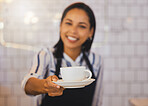 Female waiter, barista or small business owner in a coffee shop, cafe or retail shop with friendly smile and customer service. A young cashier handing cup of coffee, tea or espresso to POV consumer