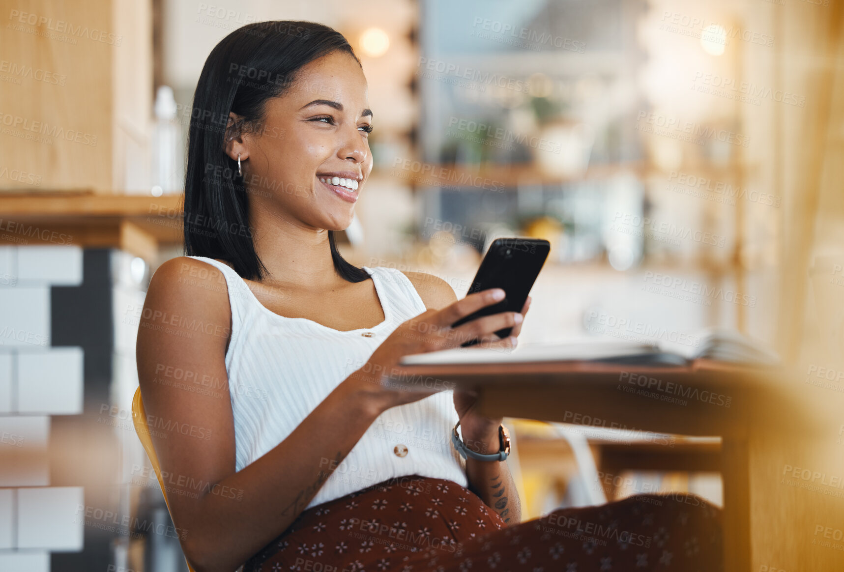 Buy stock photo Relaxing, texting a message or browsing social media on a phone by a young female student smile in a coffee shop. A happy woman thinking and searching the internet or chatting online at a cafe