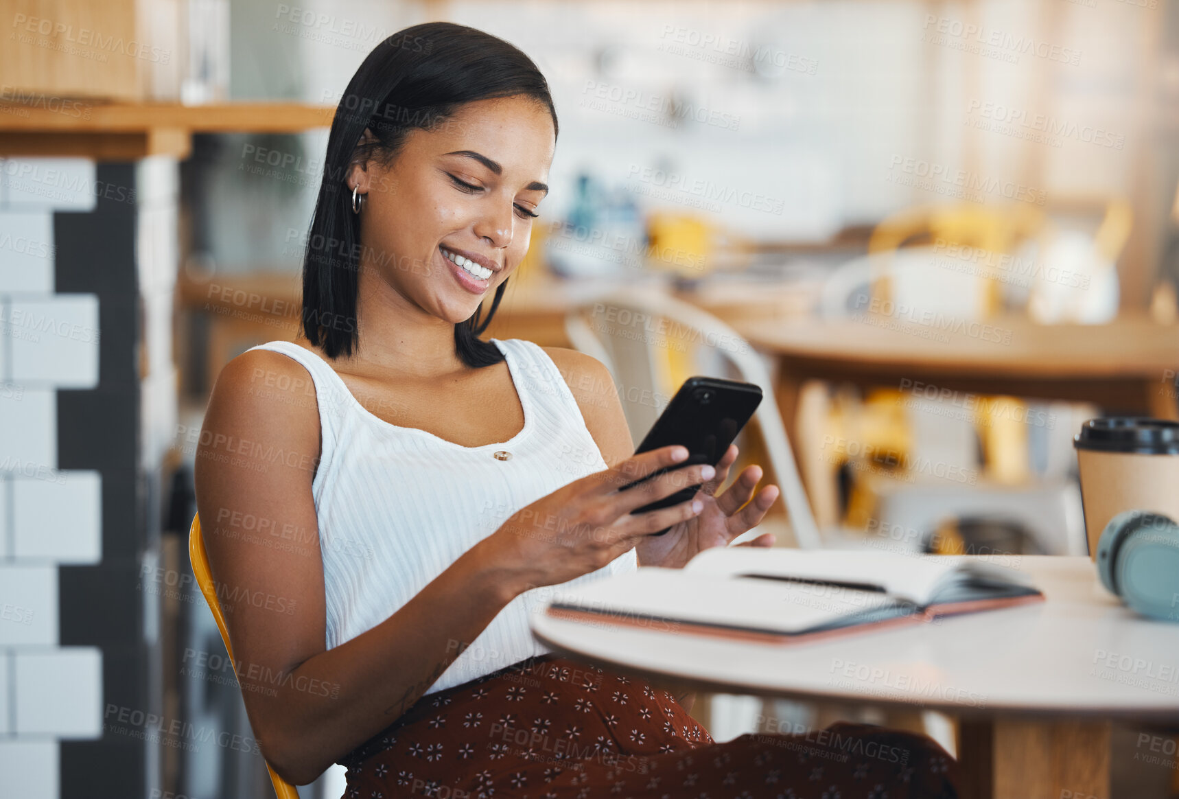 Buy stock photo Texting a message or browsing social media on a phone by a young female student sitting in a coffee shop smiling. A relaxed woman relaxing and searching the internet or chatting online at a cafe