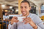 Man enjoying a cup of coffee, while smiling and sitting at a cafe relaxing. Businessman drinking tea or water at a restaurant. Young happy and attractive male holding a mug and drinking a beverage


