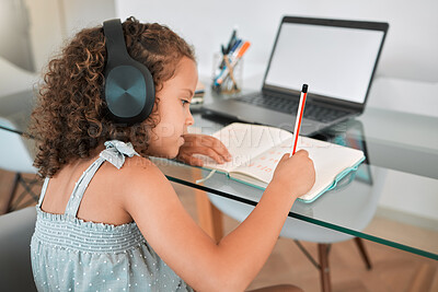 Buy stock photo Homeschooling by a smart and clever little girl attending online or virtual class using a laptop and headphones. A young child writing and working or doing homework at home listening to music