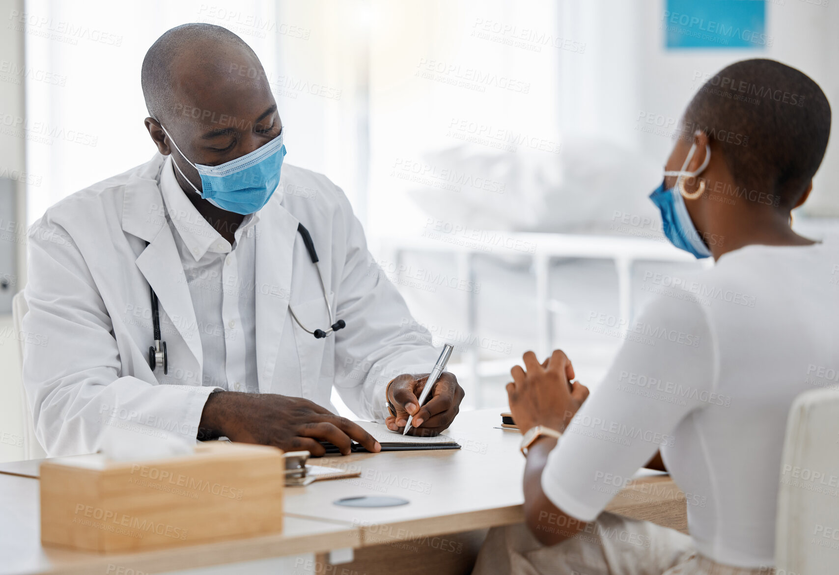 Buy stock photo Doctor, office and writing a covid note or medical history, record or insurance paperwork for patient at work. Black healthcare professional man or GP signing documents for client with masks.